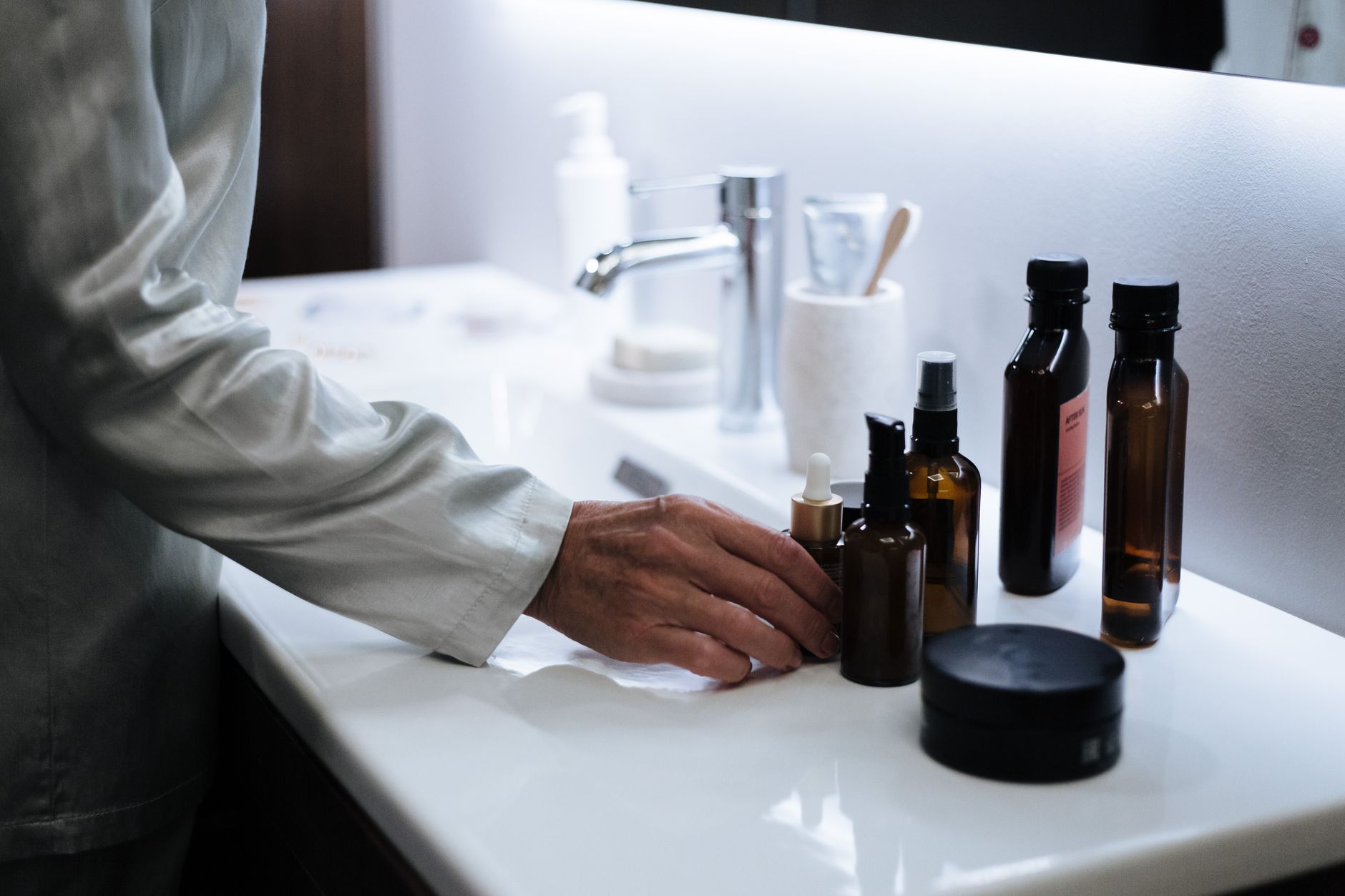 Banyo lavabosunun üzerindeki cilt bakım ürünlerine uzanan bir el