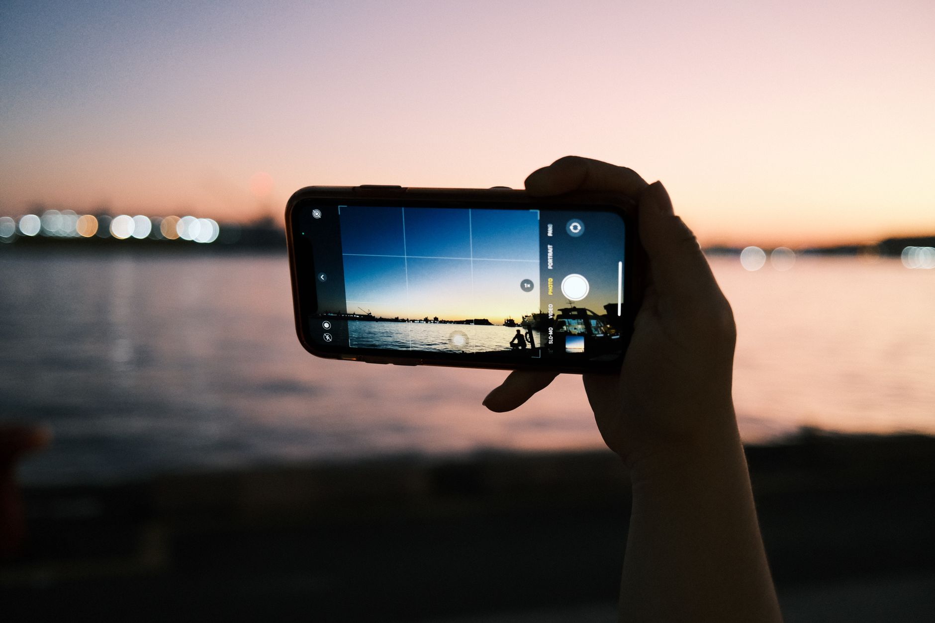 Su üzerindeki gün batımını ekranında gösteren, elle tutulan bir akıllı telefon