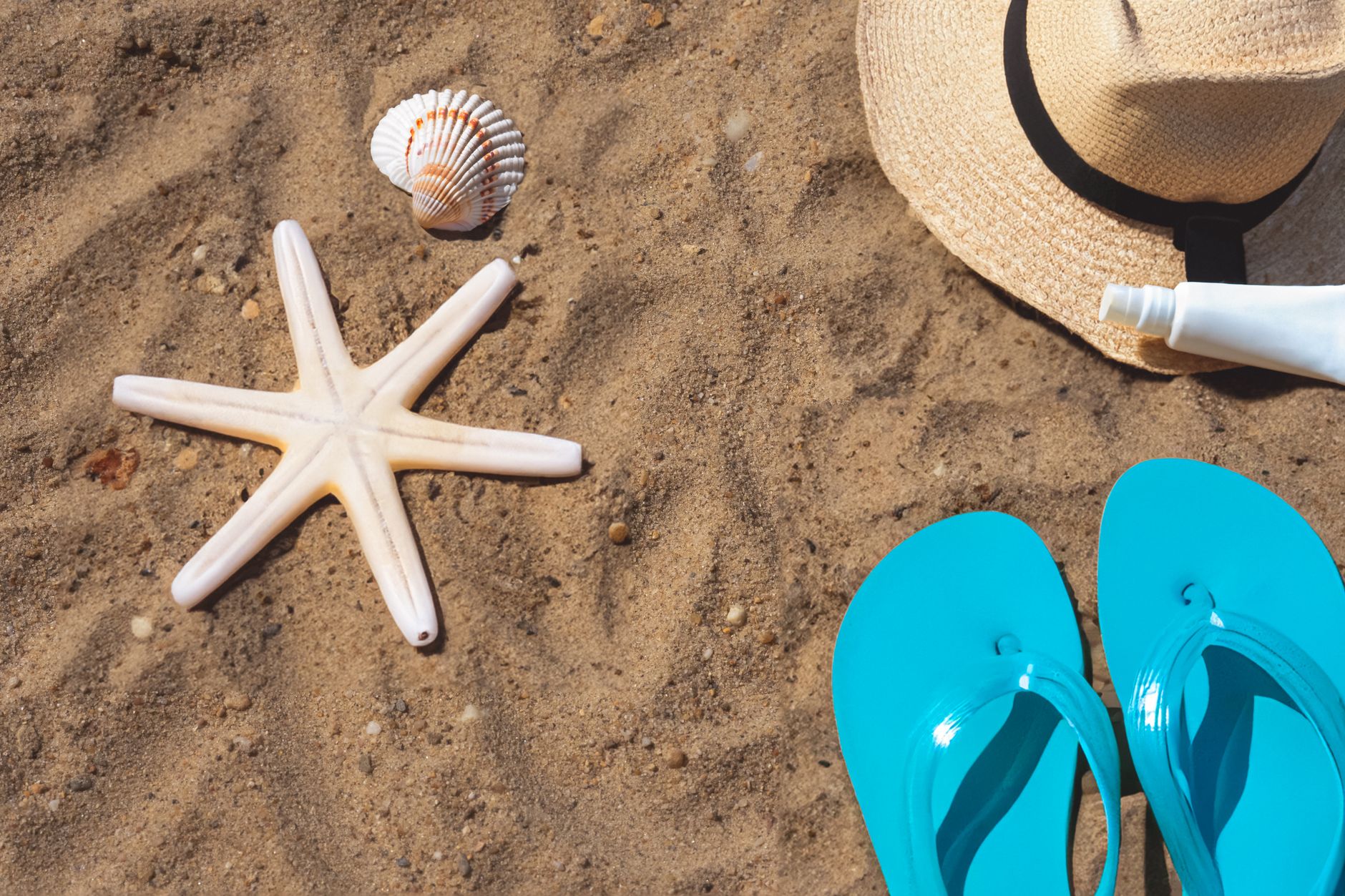 Kumun üzerinde deniz yıldızı, hasır şapka, parmak arası terlik ve güneş kremi