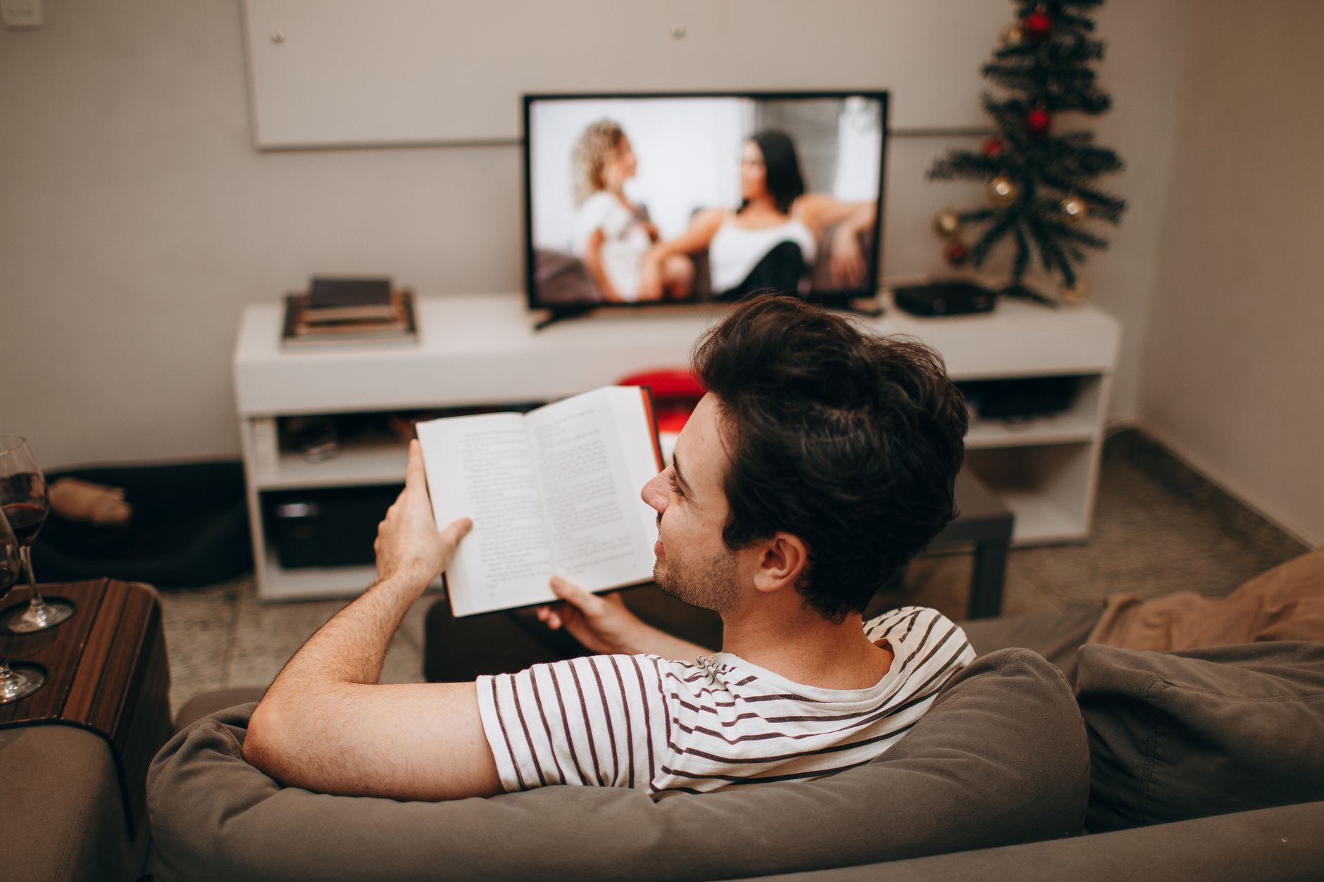 Koltukta kitap okuyan bir adam ve arkada açık televizyon