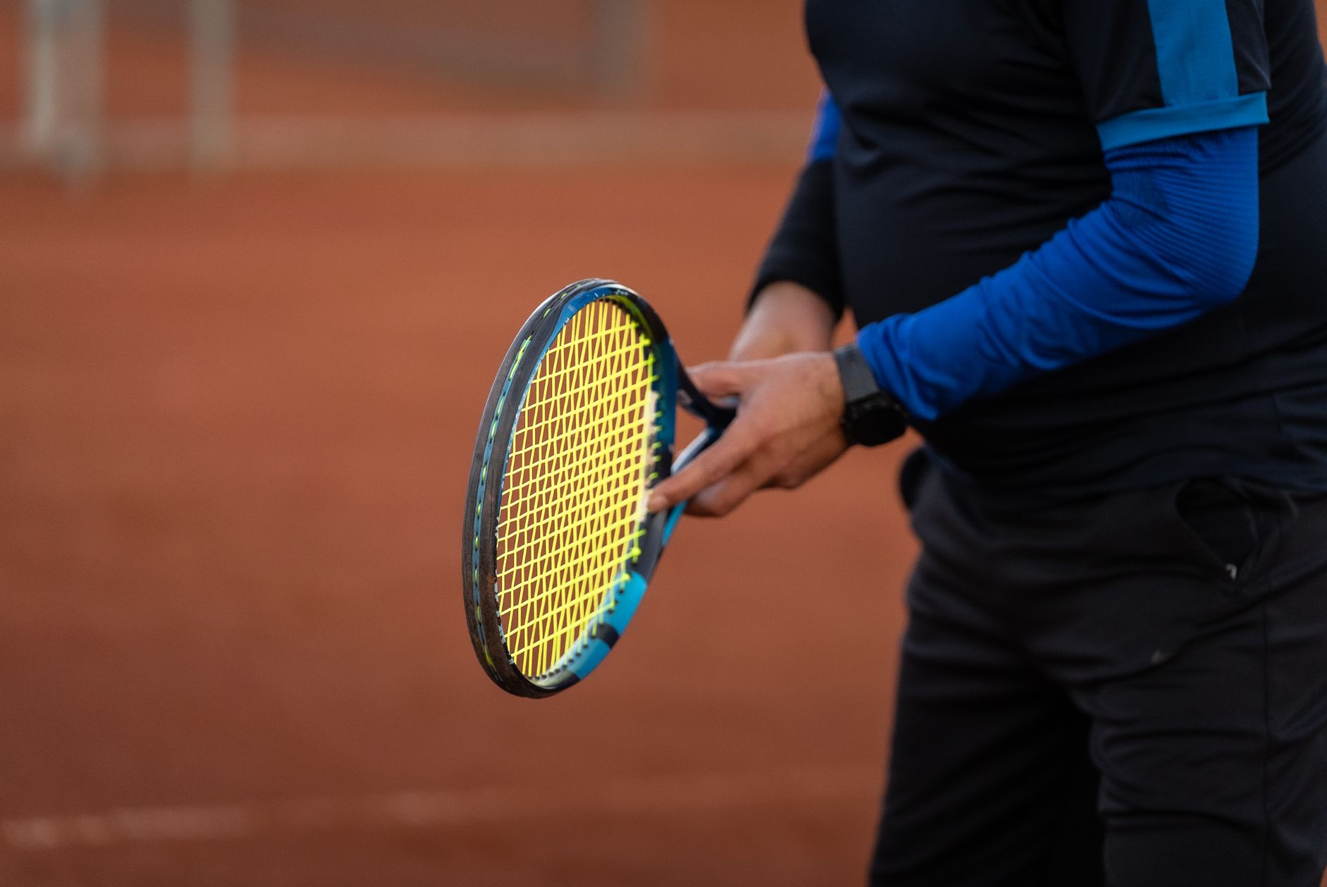 Toprak kortta tenis raketini iki eliyle kavrayan bir oyuncunun yakın çekimi