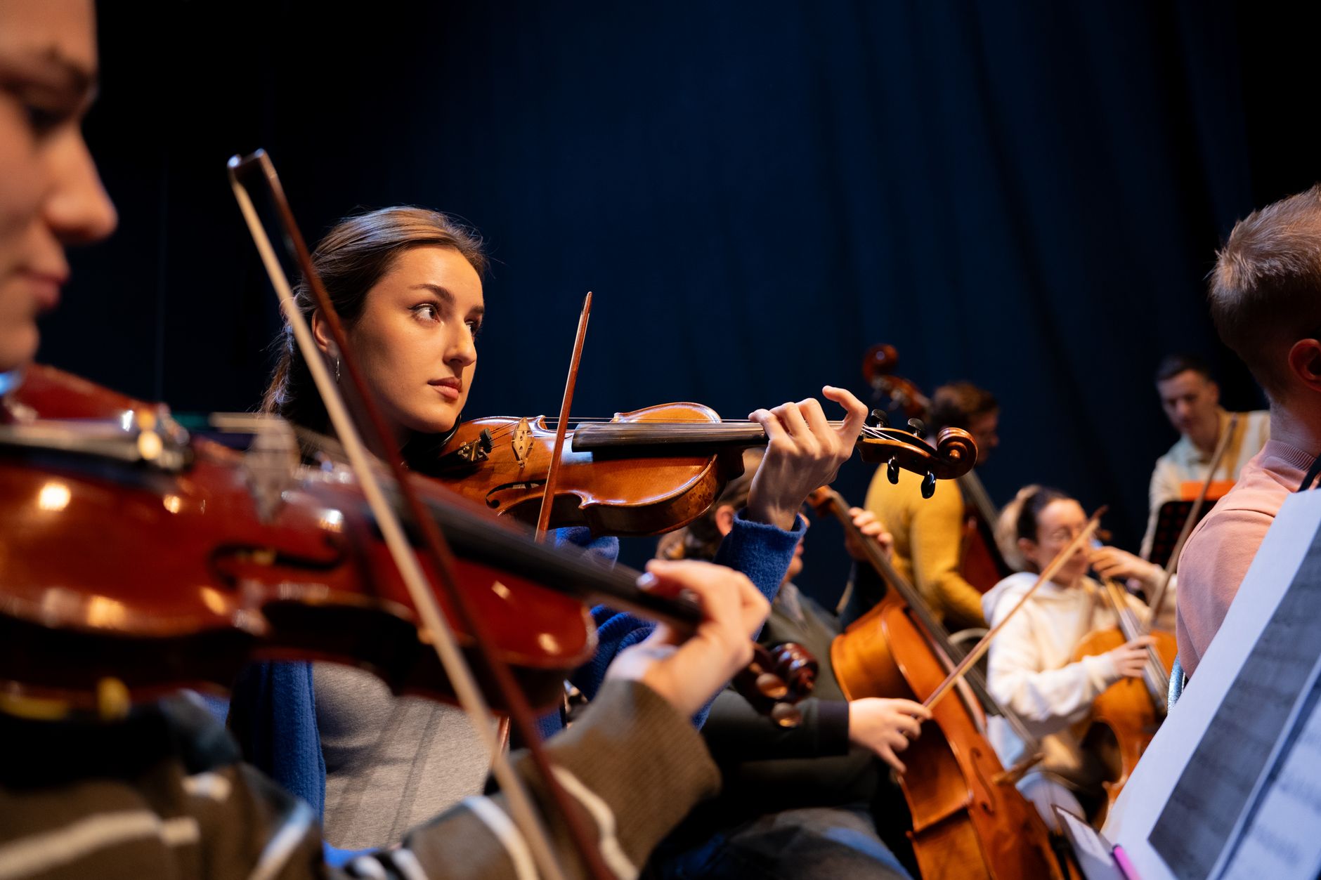 Bir orkestrada keman çalan müzisyenler, odakta bir kemancı