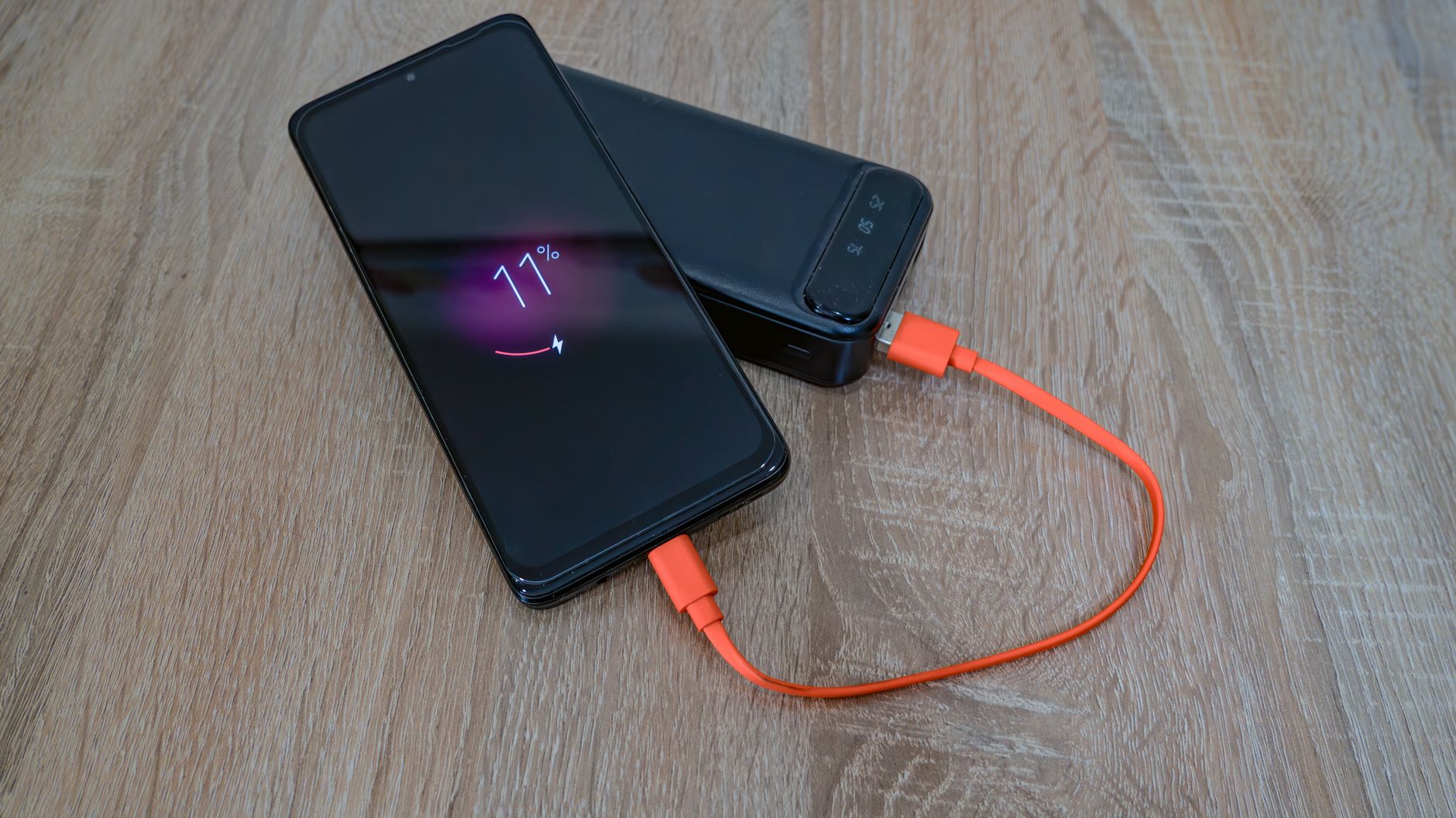 Ahşap masada turuncu kabloyla taşınabilir bataryadan şarj olan akıllı telefon