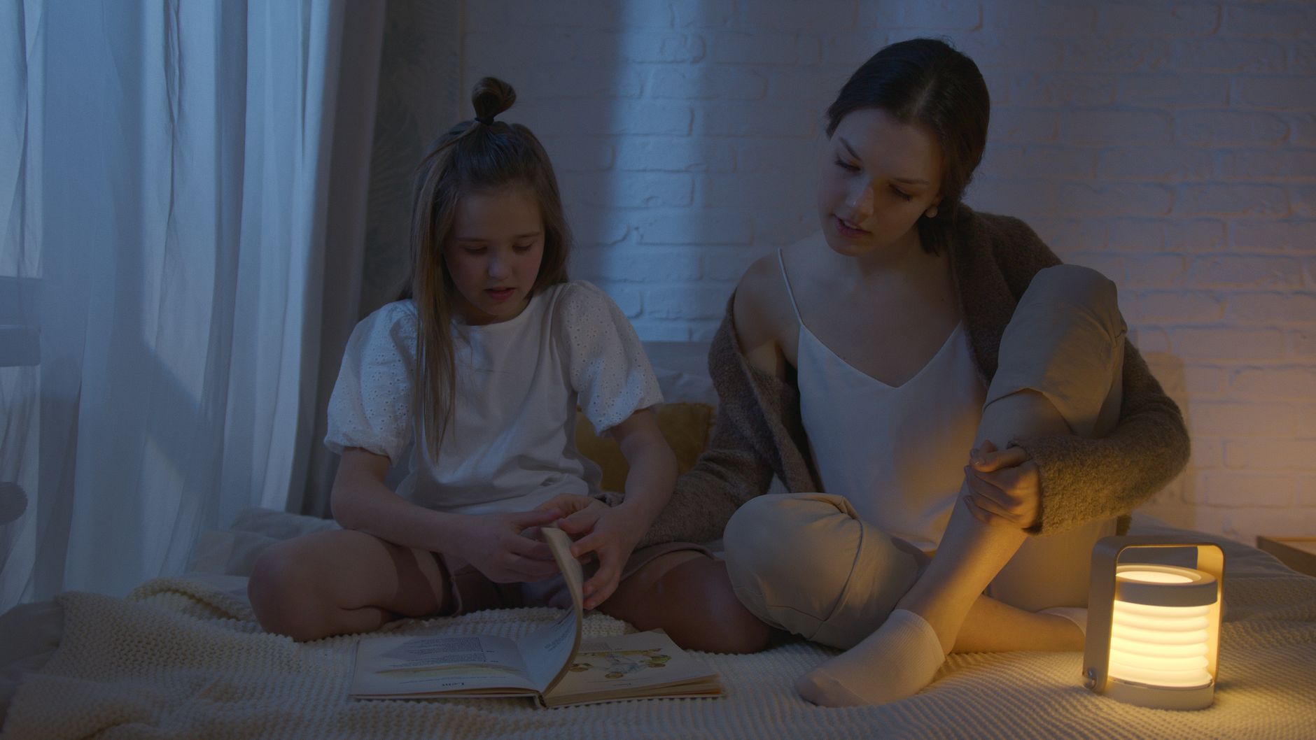 Anne ve kızı gece lambası ışığında birlikte kitap okuyor