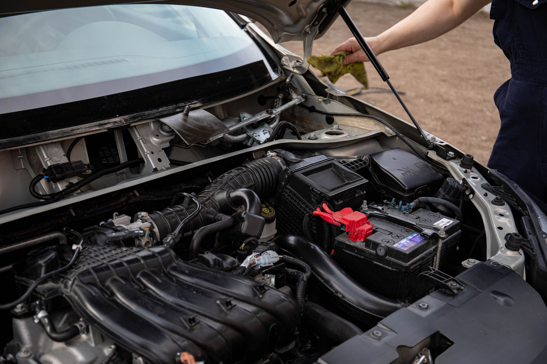 Bir teknisyenin motor bölmesinde akü ve bağlantılarını kontrol etmesi